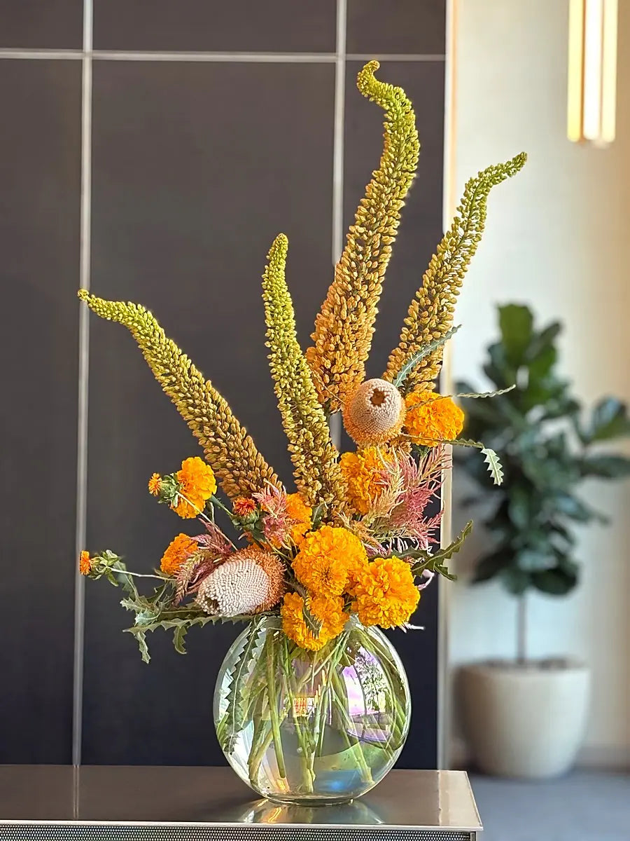 Marigolds, banksia and eremurus spires in an iridescent glass bowl