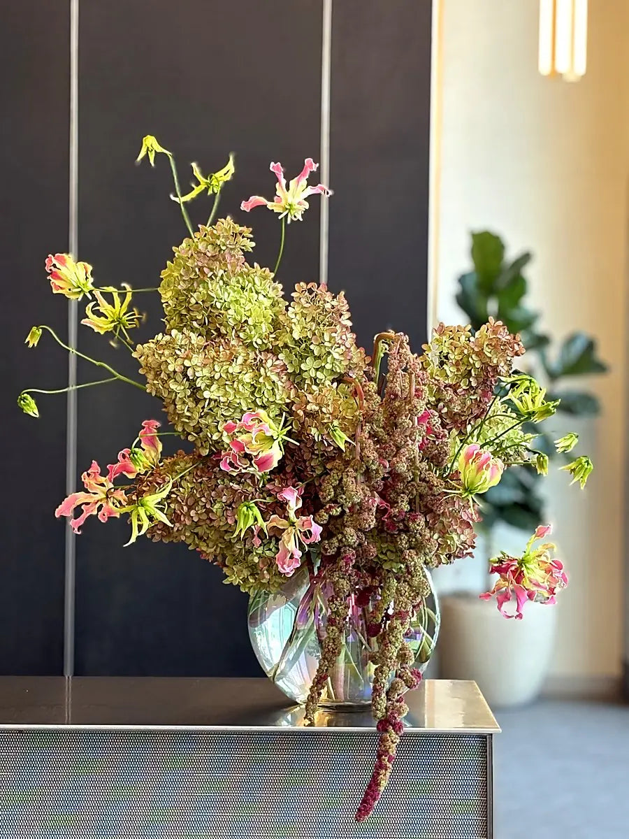 Green hydrangea, gloriosa lily and trailing amaranthus in a glass vessel on a steel console