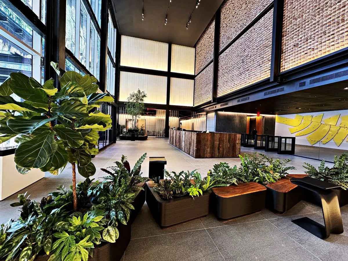 Trees and layered plants arranged along sculptural benches in a sunlit brick lobby